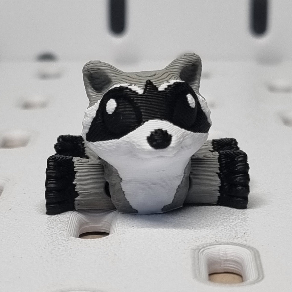 Small racoon figurine lying flat with a plain background